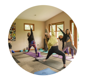 Group of people practicing yoga in a sunlit studio, standing on mats with arms raised in a stretch.